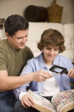 Hispanic father and son examining stamp through magnifying glass