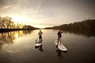 Couple paddling in river on surfboards