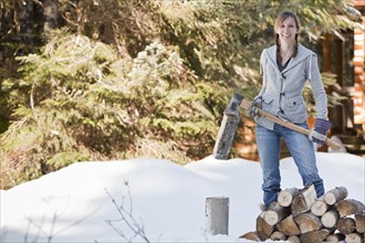 Caucasian woman chopping firewood in snow