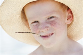 Freckled boy in hat chewing on straw