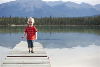 Caucasian boy walking on dock over remote lake