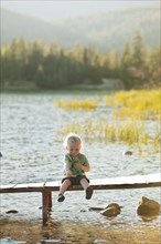 Caucasian boy sitting on wooden deck over lake