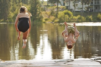 Caucasian children jumping into lake