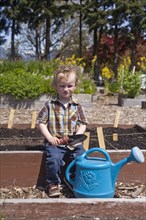 Caucasian boy holding spade with watering can in garden