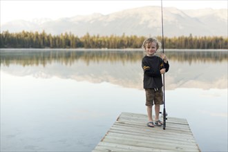 Caucasian boy standing on dock at lake holding fishing rod
