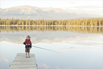Caucasian boy standing on dock at lake holding fishing rod
