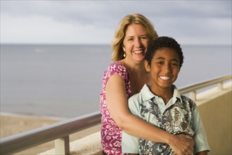 Woman hugging boy on balcony overlooking beach
