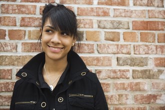 Hispanic teenage girl smiling against brick wall