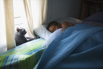 Mixed race boy sleeping in bed with cat
