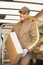 Smiling Hispanic delivery man holding cardboard box
