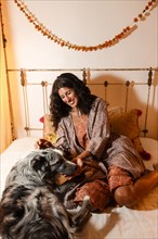 Hispanic woman sitting on bed petting dog