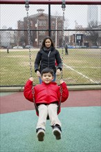 Mother pushing son on swing at playground