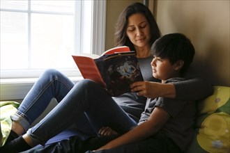 Mother and son reading book near window