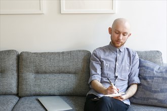 Caucasian man sitting on sofa writing in notepad