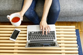 Hands of mixed race woman using laptop and drinking tea