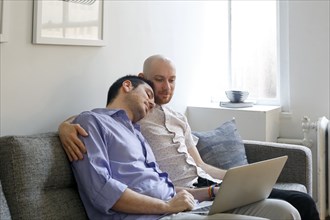 Caucasian men hugging on sofa and using laptop