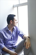 Pensive Caucasian man sitting on windowsill