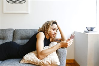 Mixed race woman laying on sofa texting on cell phone