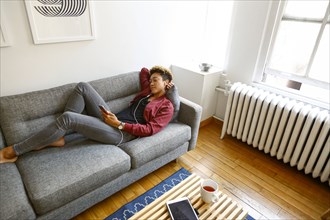 Mixed race woman laying on sofa listening to earbuds