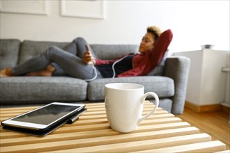 Mixed race woman laying on sofa listening to earbuds
