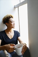 Mixed race woman drinking coffee on windowsill