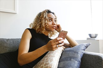 Mixed race woman laying on sofa holding cell phone