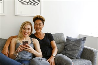 Women sitting on sofa texting on cell phone