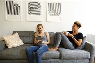 Women drinking coffee and using digital tablet on sofa