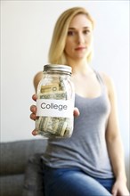 Caucasian woman showing jar of money for college