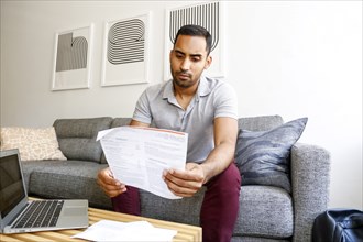 Mixed race man sitting on sofa reading paperwork