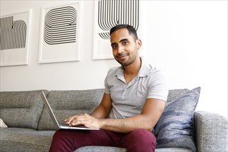 Mixed race man sitting on sofa using laptop