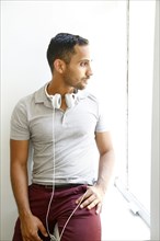Pensive mixed race man with headphones sitting on windowsill