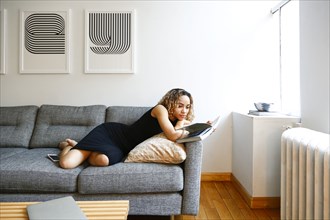 Mixed race woman laying on sofa reading book