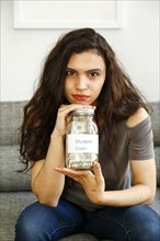 Portrait of mixed race woman holding jar of money for student loan