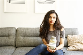Portrait of mixed race woman holding jar of money for college