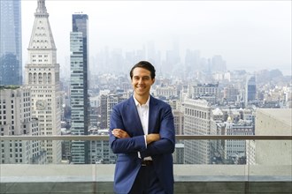 Portrait of smiling Caucasian businessman leaning on urban rooftop