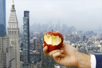 Hand of Caucasian man holding bitten apple on urban rooftop