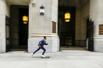 Caucasian businessman skateboarding on urban sidewalk