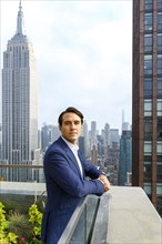 Portrait of serious Caucasian businessman leaning on urban rooftop