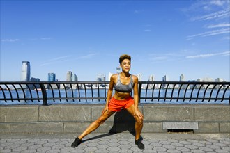 Mixed race woman stretching legs at waterfront
