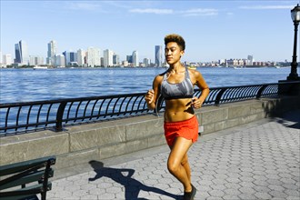 Mixed race woman running at waterfront listening to earbuds