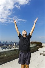 Caucasian man standing with arms raised on urban rooftop