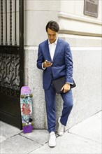Caucasian businessman with skateboard texting on cell phone