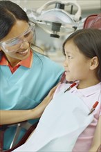 Indian female dental assistant smiling at young Asian female patient