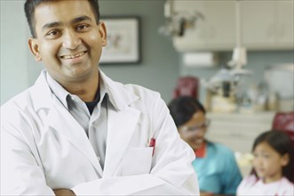 Indian male dentist with assistant and patient in background