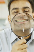 Indian man holding up magnifying glass to his teeth with braces