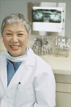 Senior Asian female dentist smiling next to x-rays