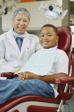 Senior Asian female dentist and African boy in dentist's chair