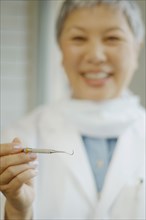 Senior Asian female dentist holding up dental tool