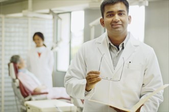 Indian male dentist with patient in background
